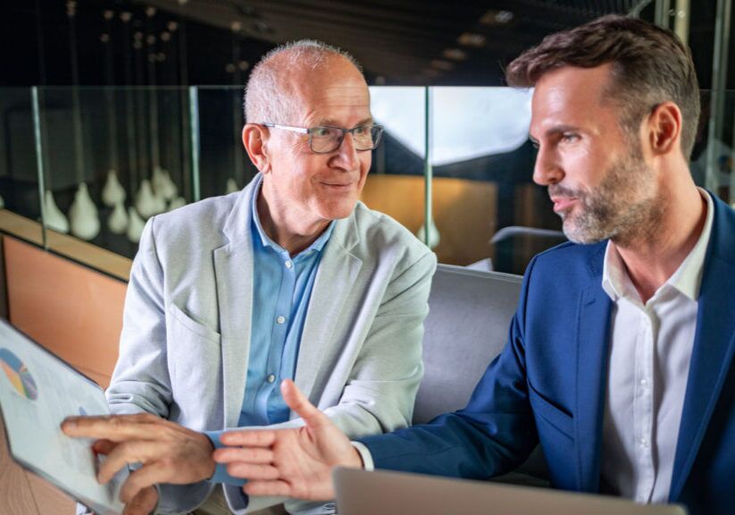 Younger and older businessman talking about documents during meeting in modern business lounge