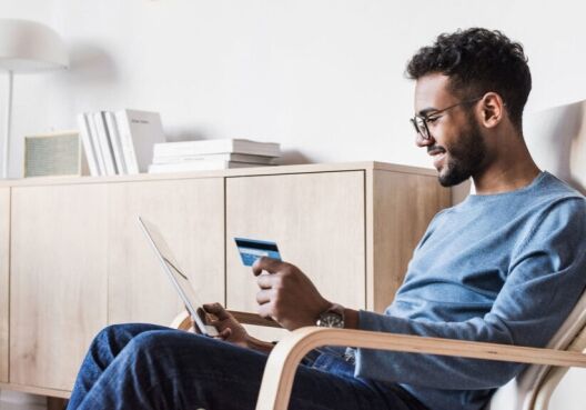 Young man holding credit card while reading on laptop